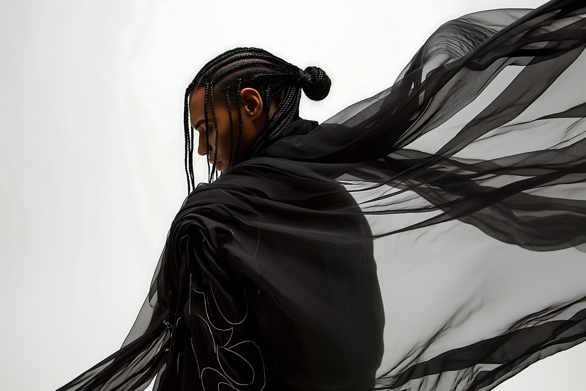 A model with braided hair in black sheer fabric flowing in the wind