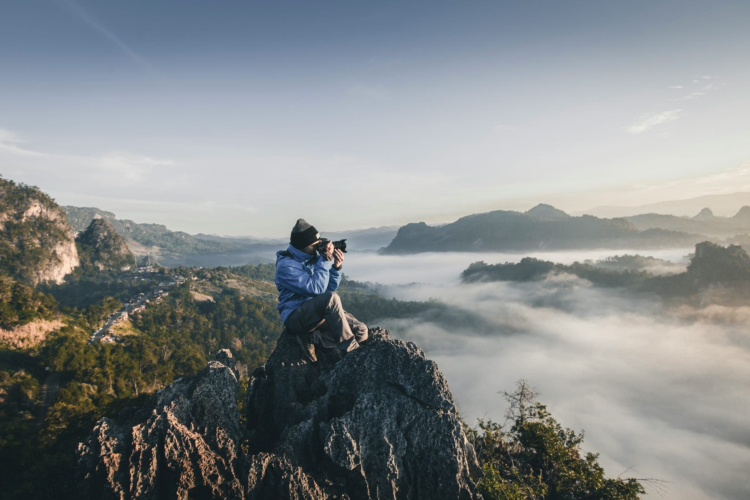 A photographer on a rocky peak shooting a valley filled with fog